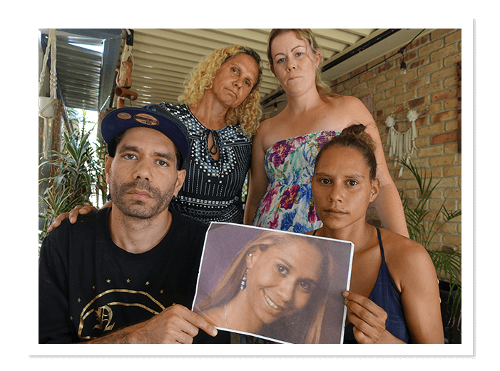 Two women standing, one man and woman sitting holding photograph of you missing indiegnous woman.