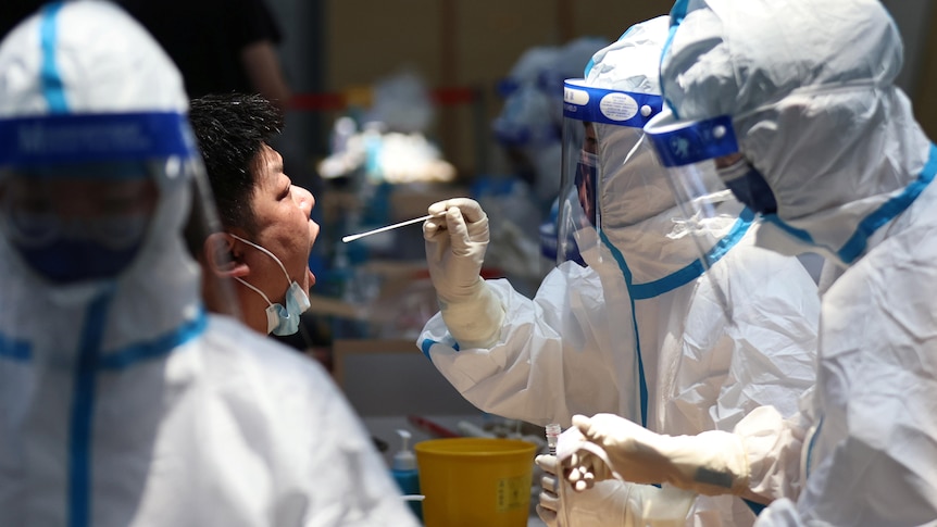 A man opens his mouth while a health worker in full PPE holds a swab in front of his face 