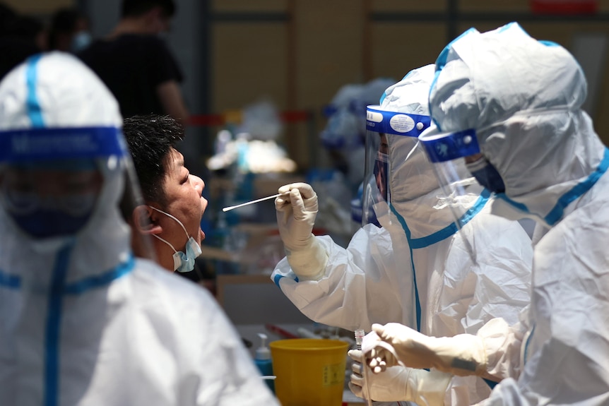 A man opens his mouth while a health worker in full PPE holds a swab in front of his face 