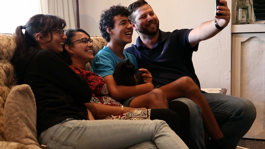 A family seated on a couch take a 'selfie'