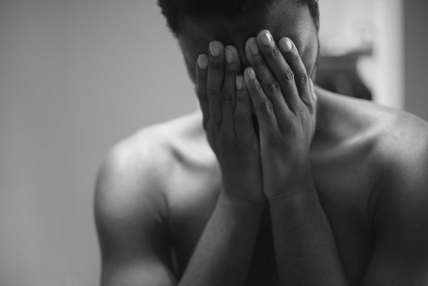 A black and white photo of a topless young man who is covering his face to hide his identity to depict safe sexting.