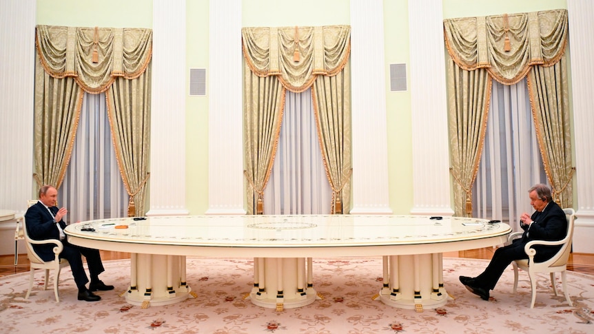 Two middle aged men seated opposite each other at a very long white table.