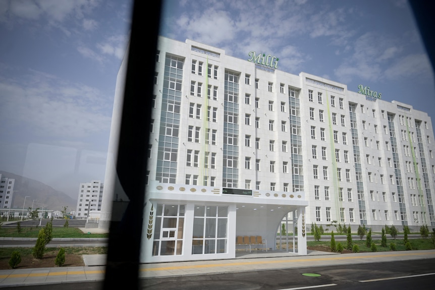 A large white apartment block sits behind a pristine white bus stop.
