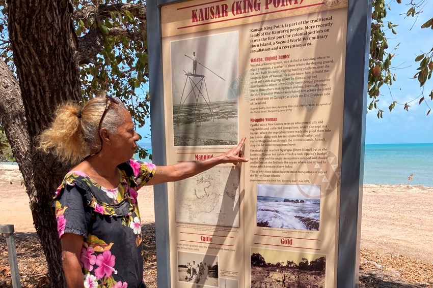 Elderly Indigenous woman reading large sign near beach 