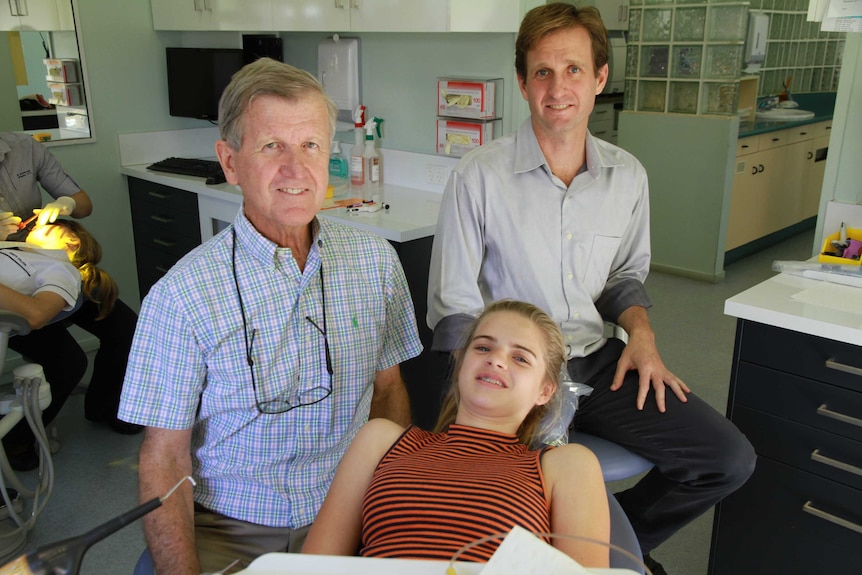 Dr Nicholas Manning and his father Dr Michael Manning sit on stools as a young female patient waits for her examination.