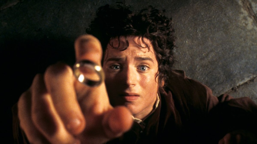 A man with bright blue eyes and dark curly hair reaching desperately for a gold ring.