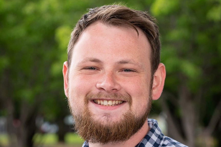 A young man with brown hair and a brown beard smiles at the camera