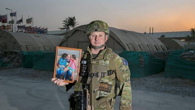 Sands Skinner holds a photo of his children while dressed in military uniform at Afghanistan.