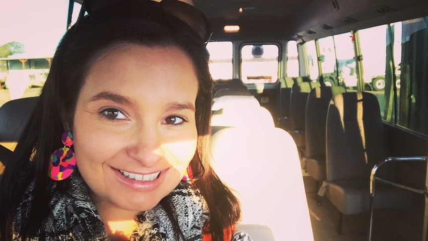 Woman with big earrings and sunglasses on her head sits in driver's seat of small bus