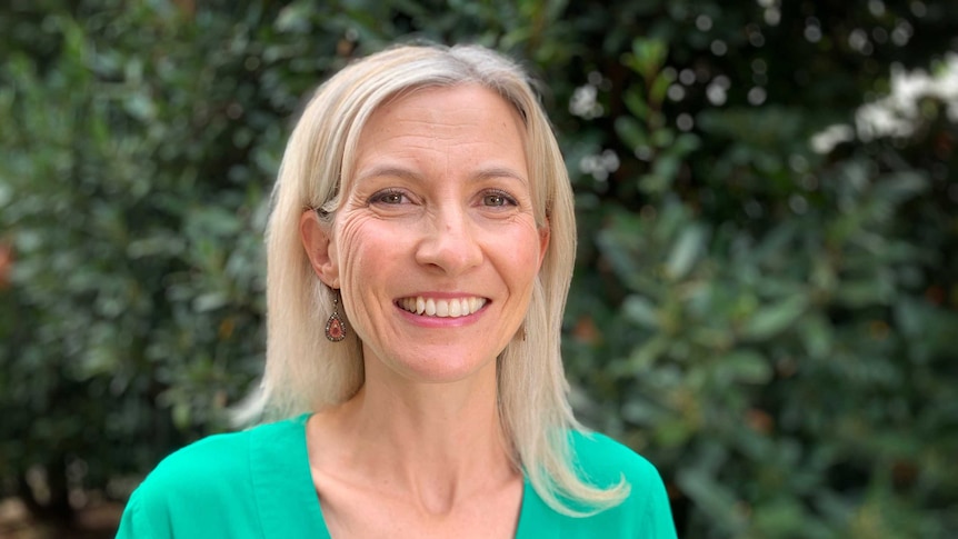 A blonde woman stands smiling at camera while wearing aqua top