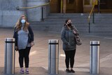 Two people wearing face masks wait on the street outside a quiet Flinders Street Station