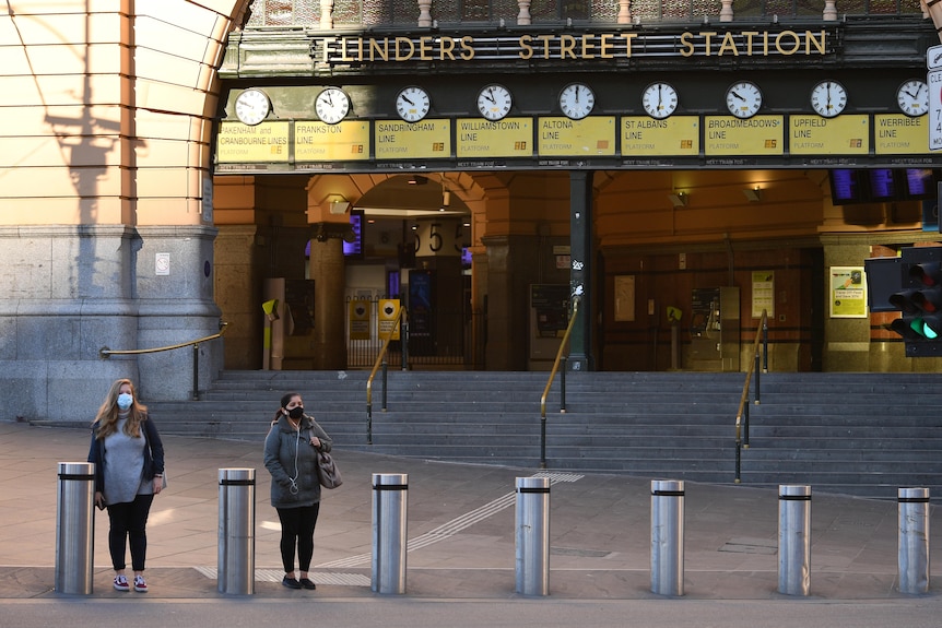 Two people wearing face masks wait on the street outside a quiet Flinders Street Station