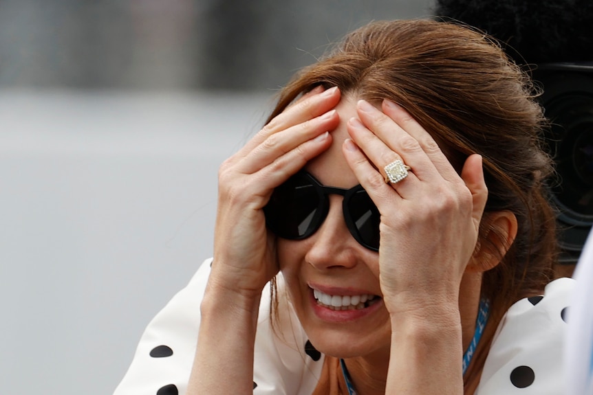 Emma Dixon holds her head and grimaces while wearing sunglasses