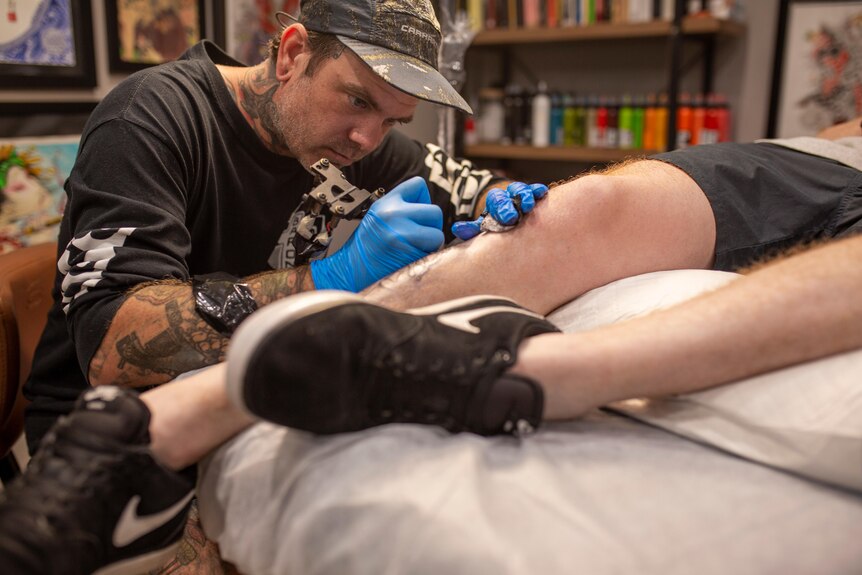 A man tattooing the calf of a person lying on a bed