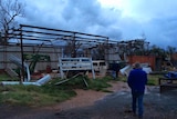 Man looks at destroyed shed with farm equipment