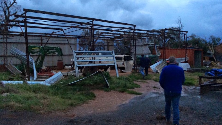 Man looks at destroyed shed with farm equipment