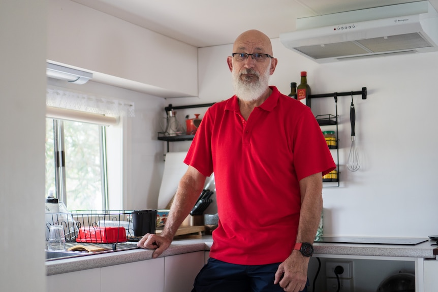 A man with a white beard stands in his kitchen.