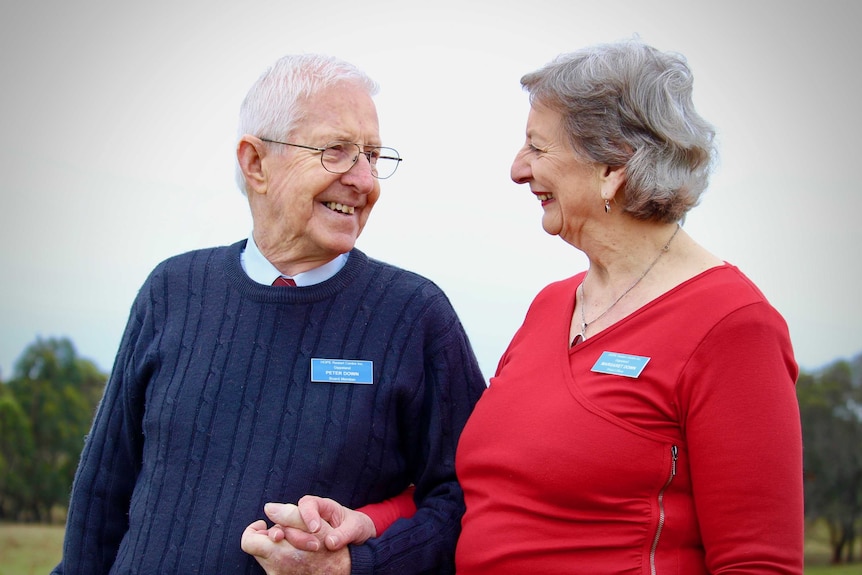 An older couple holding hands and smiling at each other