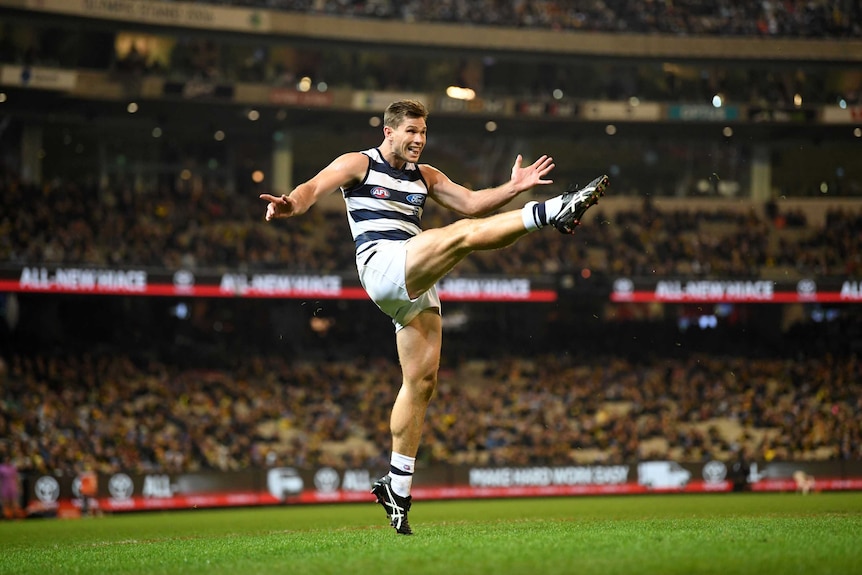 An AFL forward in full extension kicking for goal at the MCG.