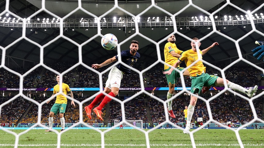 The ball heads towards the net for a goal after a header from a French striker with two Australian defenders watching.
