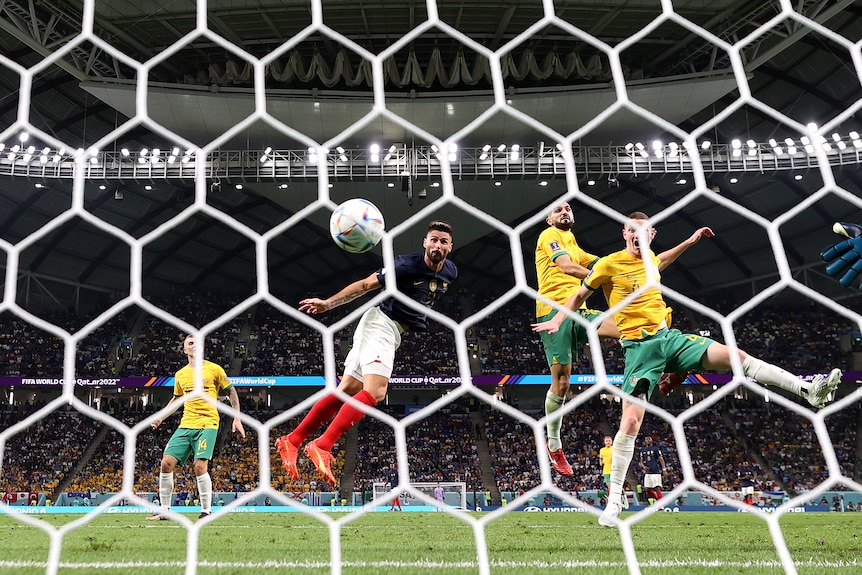 The ball heads towards the net for a goal after a header from a French striker with two Australian defenders watching.