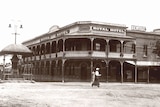 An historic black and white photo of an old pub with a woman walking across in the foreground 