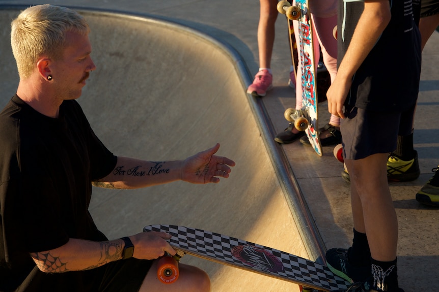 Jayden Sheridan holds a skateboard for a young child preparing to go down the ramp.