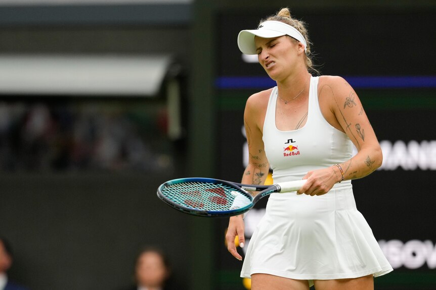 A tennis player grimaces as she looks down at her racquet during a grasscourt match at Wimbledon.