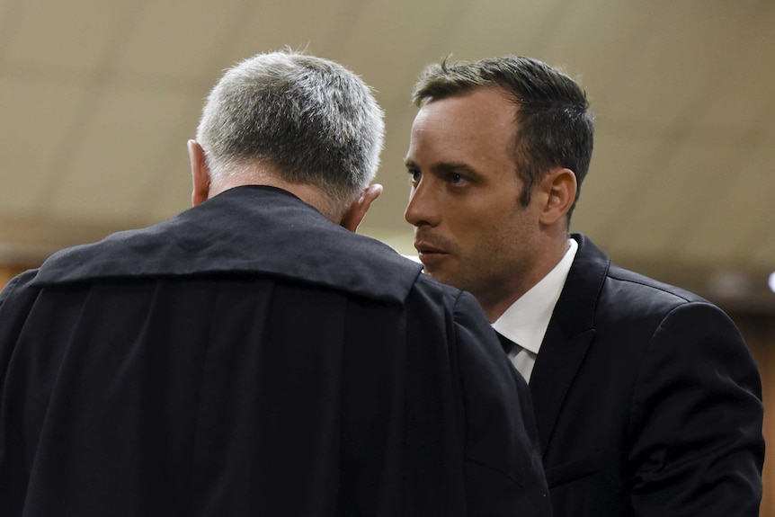 Oscar Pistorius (R) speaks to his lawyer Barry Roux