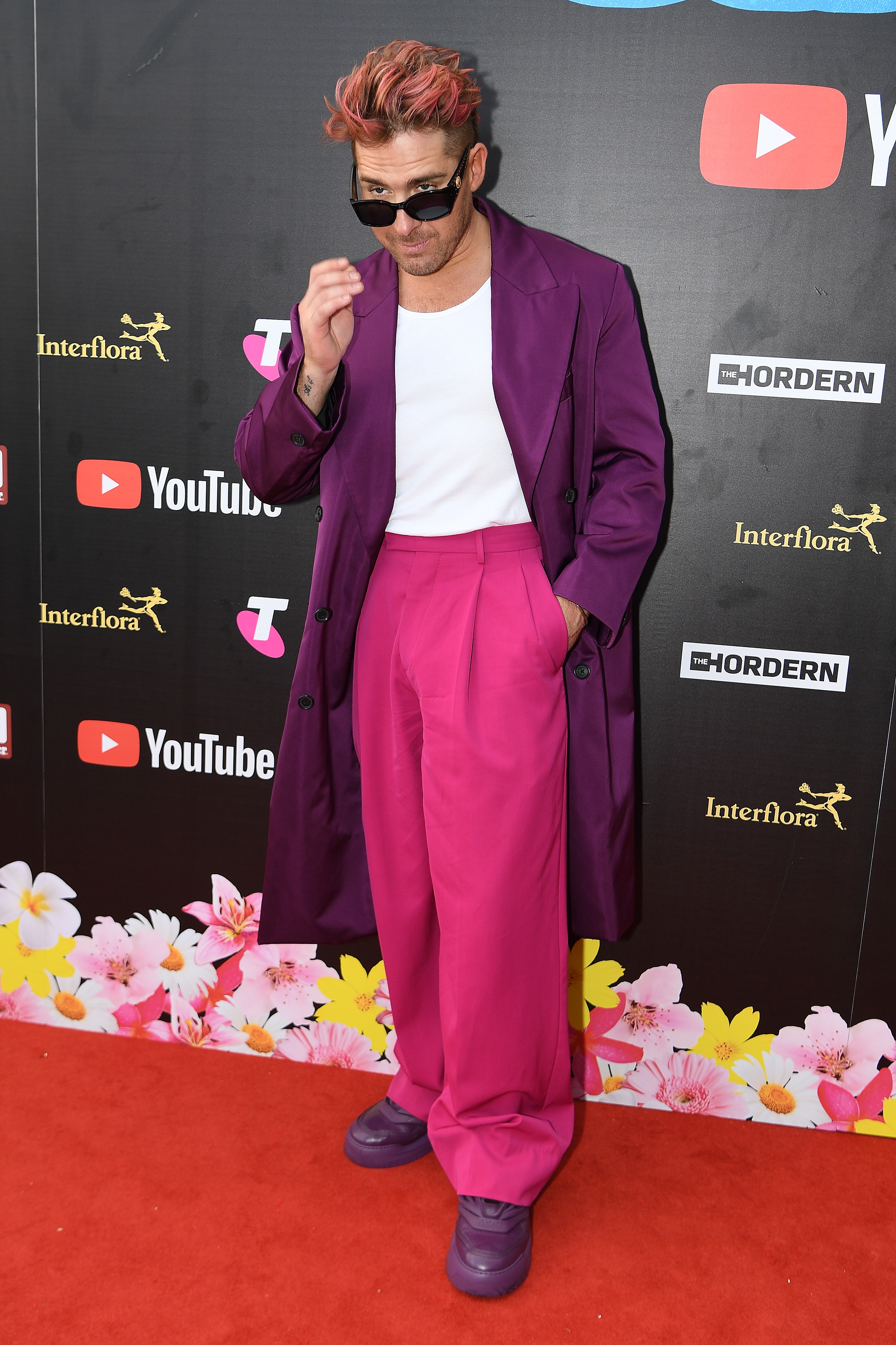 Hugh Sheridan portant une veste de costume violette, un haut blanc et un pantalon rose vif