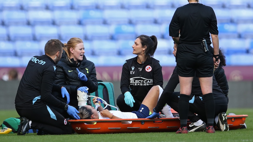 Tottenham Hotspur's Kyah Simon lies on a stretcher as trainers crouch around her.