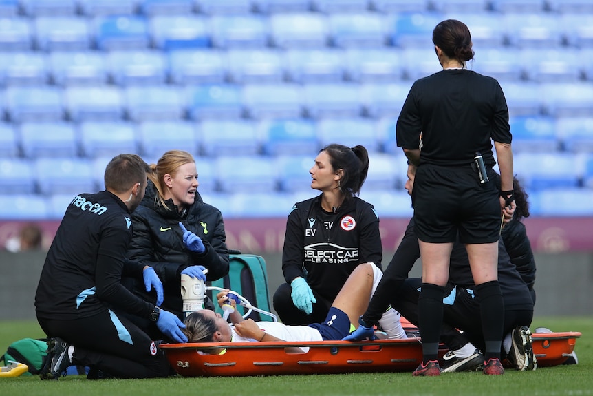Tottenham Hotspur's Kyah Simon lies on a stretcher as trainers crouch around her.