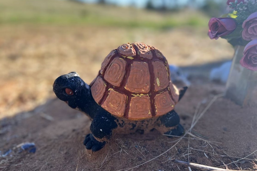 A turtle statue stands beside flowers on a grave.