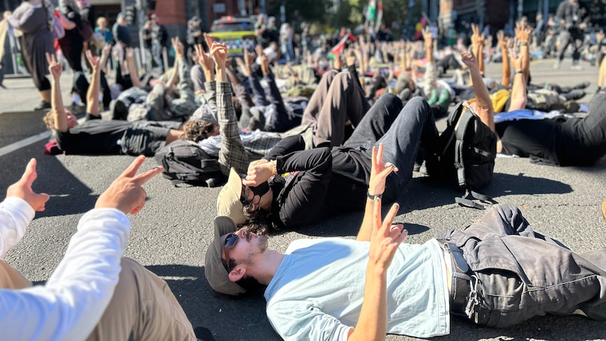 Dozens of protesters lie down on the corner of Spencer and Bourke streets.