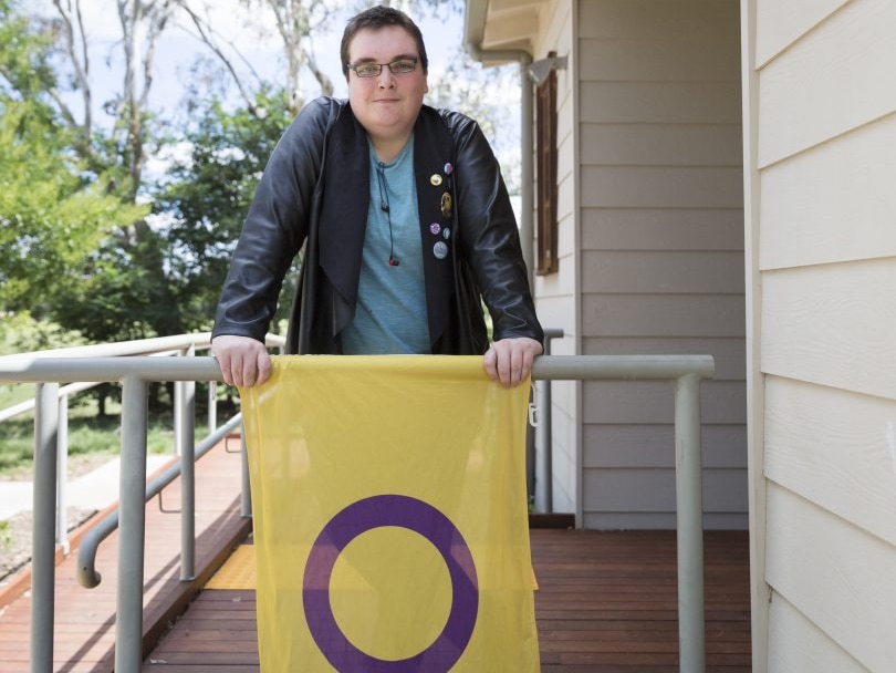 Cody Smith with the intersex flag, which is a purple circle on a yellow background.