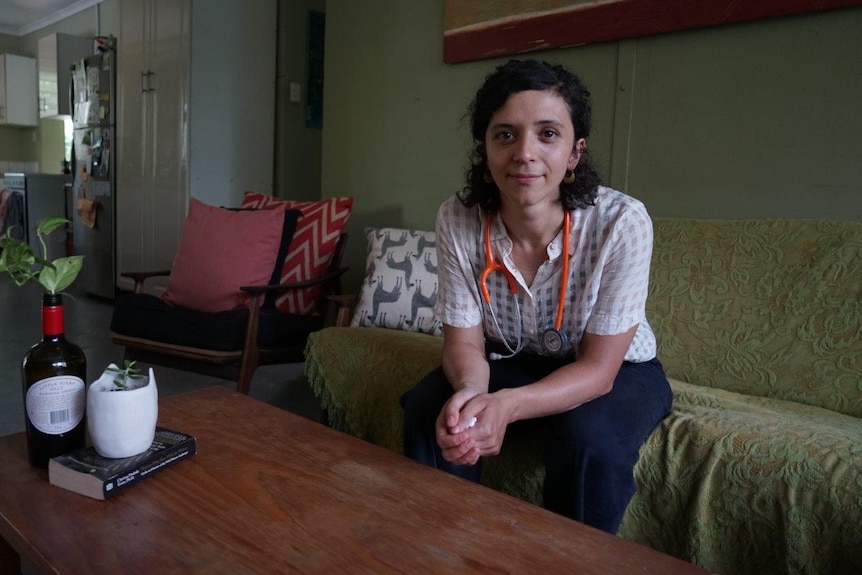 A woman wearing a stethoscope sits on a couch