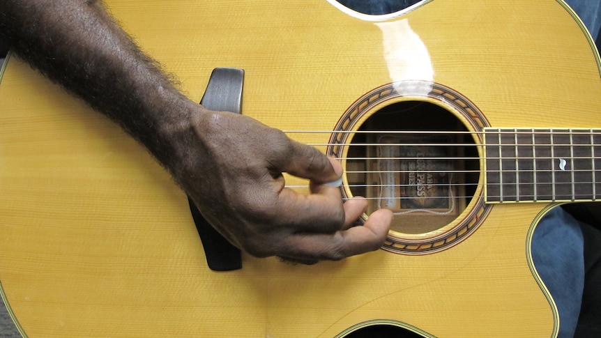A man's hand strums a guitar