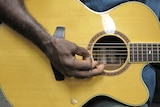 A man's hand strums a guitar