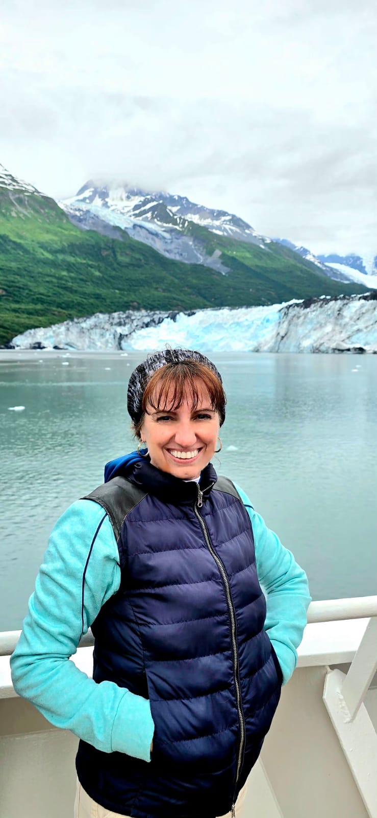 A woman in a beanie stands next to some ice caps and freezing water hole.