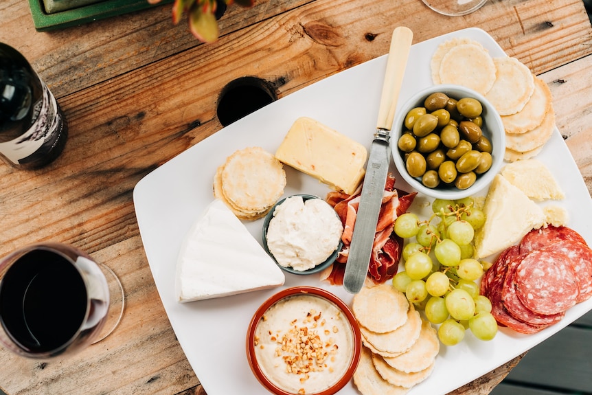 Aerial view of cheese, dips and biscuits on a platter, bottle of red wine and filled glass beside