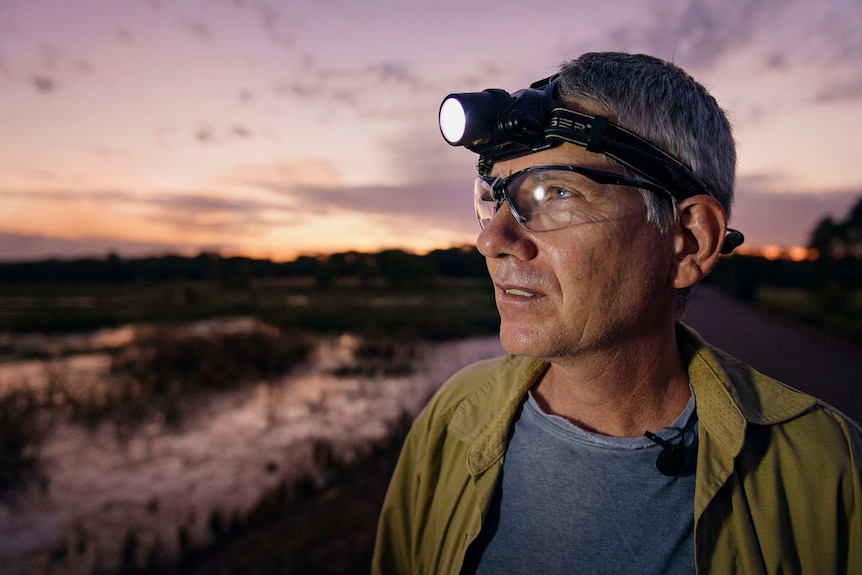 Dr Greg Brown looks across the Fogg Dam landscape wearing a head torch at dusk.