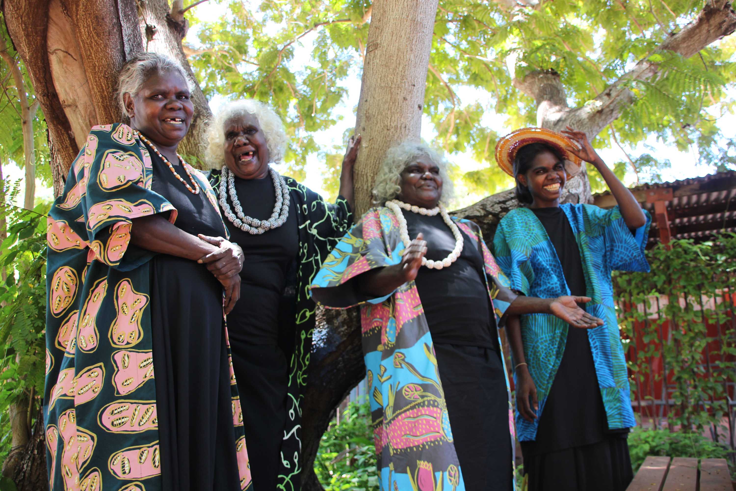 Four Aboriginal women wearing brightly-coloured fabrics and laughing.