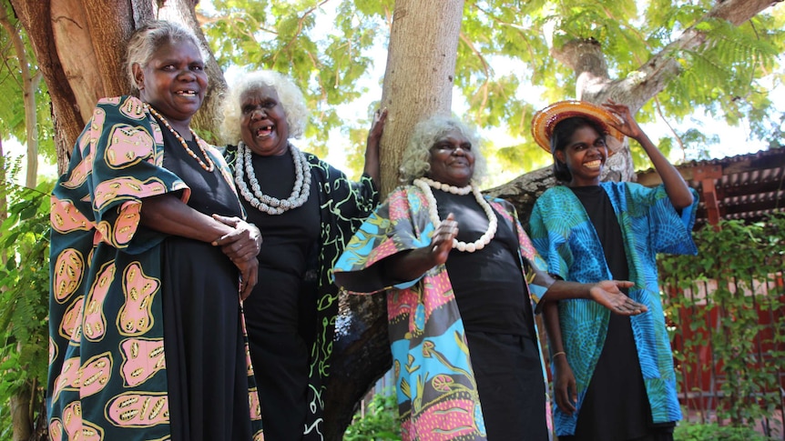 Four Aboriginal women wearing brightly-coloured fabrics and laughing.