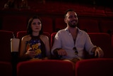 Chloe Bayliss as Amy on a date in a movie theatre. She looks serious holding popcorn, while her date is smiling.
