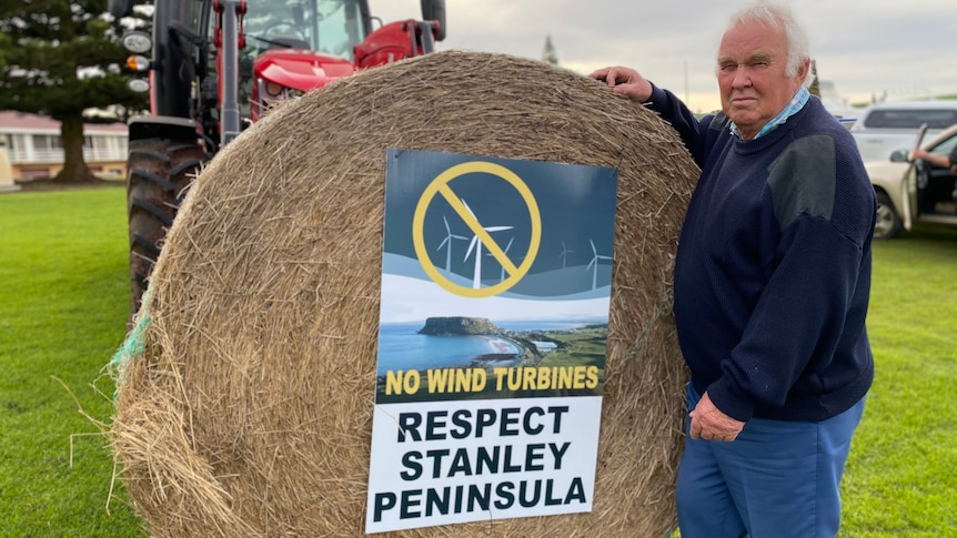 A man next to a tractor and a hay bale.