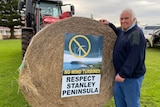 A man next to a tractor and a hay bale.