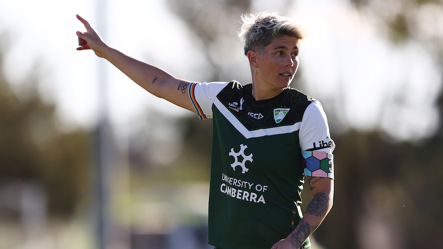 A woman soccer player wearing green, white and black shirt points to the sky during a game