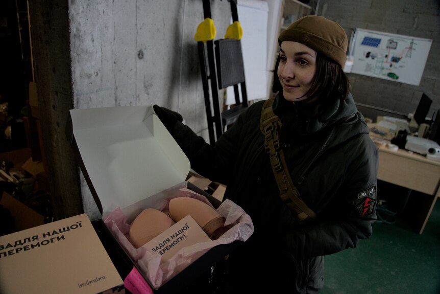 A woman in military uniform holds a box containing a wireless bra. 
