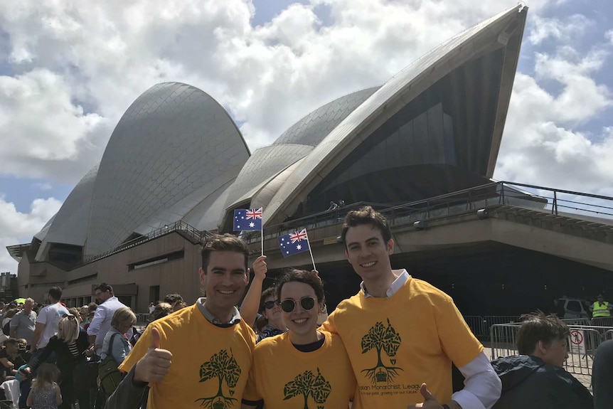 Three people wearing Young Monarchists tshirts stand outside the Opera House