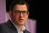 Daniel Andrews in a suit speaks behind a lectern against a purple background.